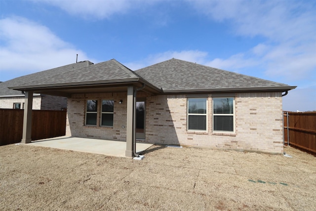 back of property featuring a patio, brick siding, roof with shingles, and a fenced backyard