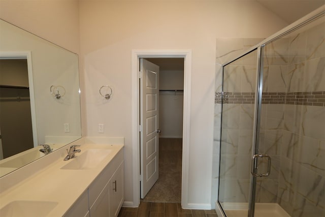 bathroom featuring double vanity, a stall shower, a sink, and a walk in closet