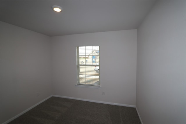 spare room with dark carpet and baseboards