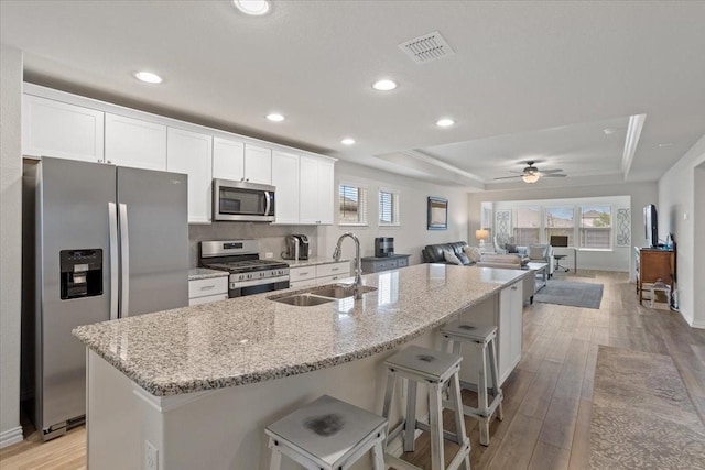 kitchen with sink, light hardwood / wood-style flooring, a center island with sink, white cabinets, and appliances with stainless steel finishes