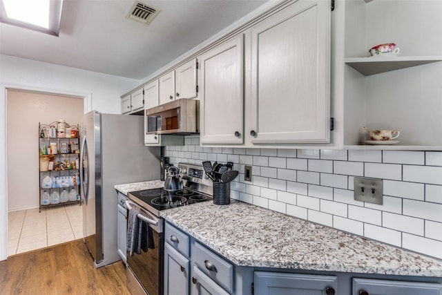 kitchen featuring light stone countertops, stainless steel appliances, blue cabinets, decorative backsplash, and hardwood / wood-style flooring