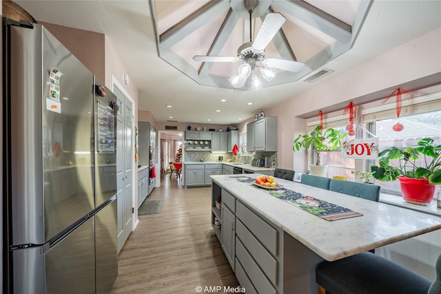 kitchen with gray cabinetry, light hardwood / wood-style flooring, stainless steel fridge, a kitchen island, and decorative backsplash