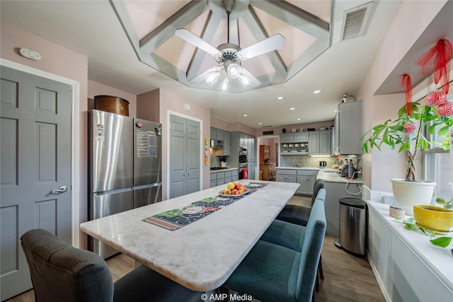 kitchen with stainless steel refrigerator, gray cabinetry, hardwood / wood-style floors, a kitchen island, and decorative backsplash