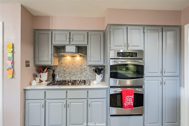 kitchen with tasteful backsplash, gray cabinets, stainless steel appliances, and wall chimney exhaust hood