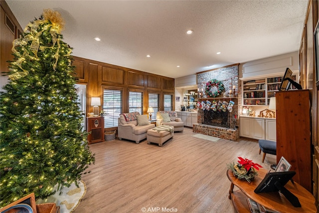 living room with light wood-type flooring, wooden walls, a fireplace, and a textured ceiling