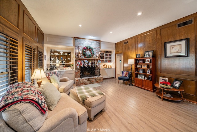 living room featuring a brick fireplace, wooden walls, built in features, and light wood-type flooring