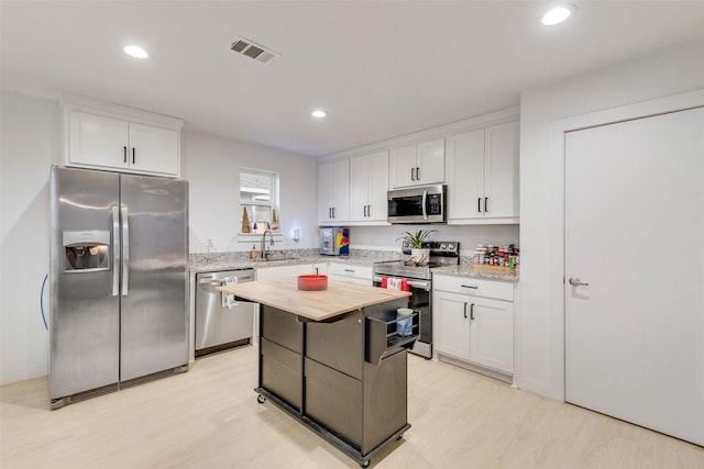 kitchen featuring appliances with stainless steel finishes, a center island, light wood-type flooring, and white cabinets