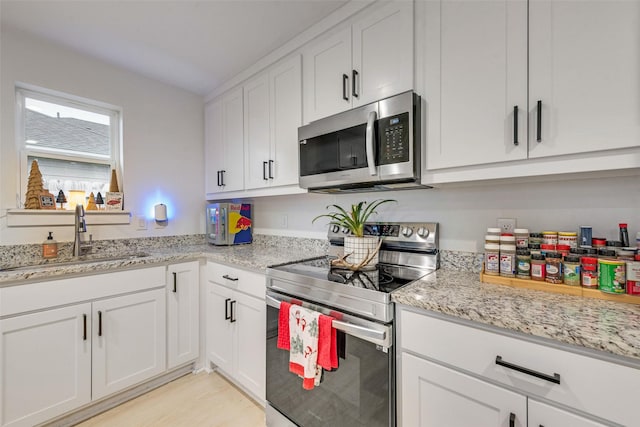 kitchen with sink, stainless steel appliances, light stone countertops, white cabinets, and light wood-type flooring