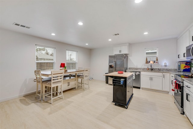 kitchen with a kitchen island, white cabinets, light stone counters, stainless steel appliances, and light hardwood / wood-style flooring