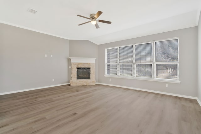 unfurnished living room featuring vaulted ceiling, a stone fireplace, ceiling fan, light hardwood / wood-style floors, and crown molding