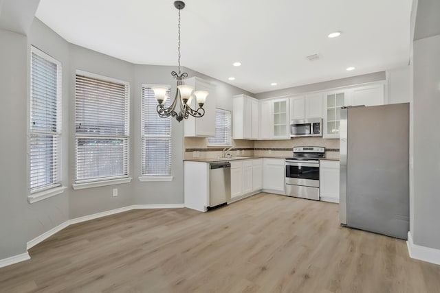 kitchen with light wood-type flooring, appliances with stainless steel finishes, pendant lighting, decorative backsplash, and white cabinets