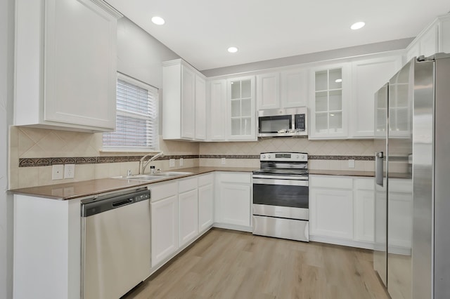 kitchen with stainless steel appliances, white cabinetry, sink, and light hardwood / wood-style floors