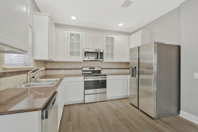 kitchen with sink, tasteful backsplash, appliances with stainless steel finishes, light hardwood / wood-style floors, and white cabinets