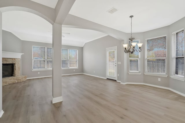 unfurnished living room featuring a stone fireplace, an inviting chandelier, and light hardwood / wood-style floors