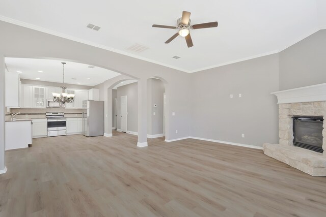 unfurnished living room featuring sink, light wood-type flooring, ornamental molding, a fireplace, and ceiling fan with notable chandelier