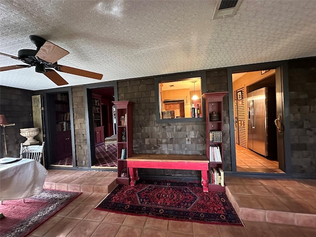 interior space featuring a ceiling fan, concrete block wall, visible vents, and a textured ceiling