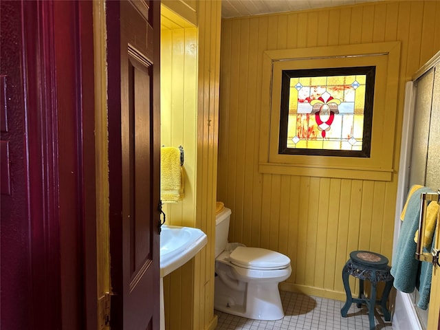 half bathroom featuring wooden walls, toilet, and tile patterned floors