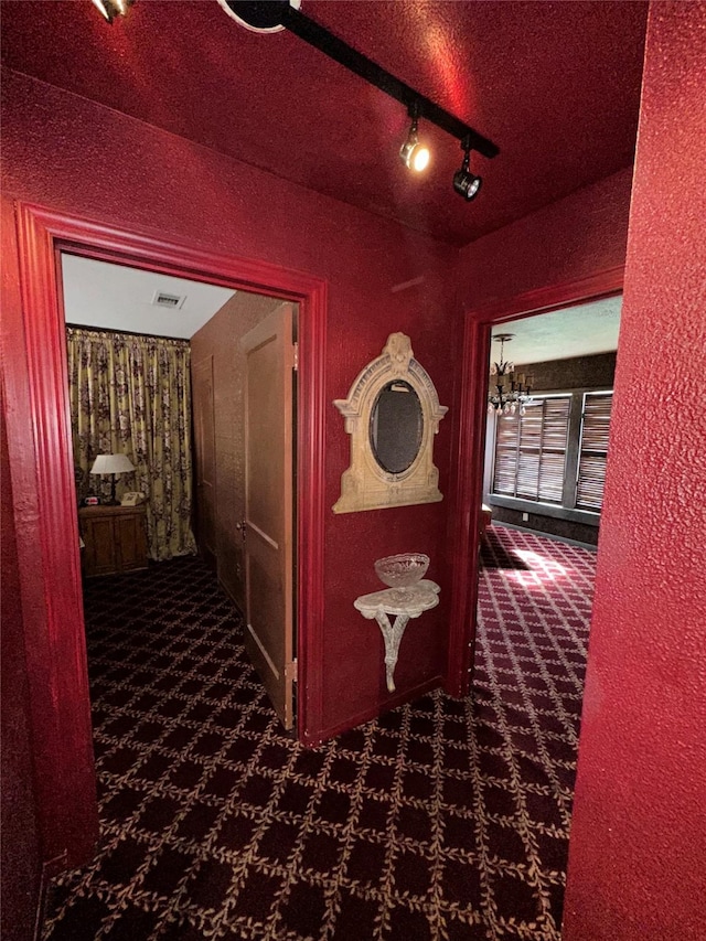 hallway with rail lighting, visible vents, dark colored carpet, and a textured ceiling