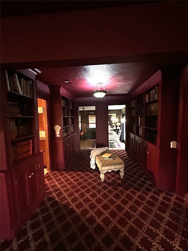 interior space with visible vents, built in shelves, dark carpet, and a textured ceiling