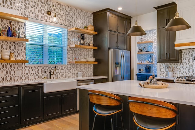 kitchen with backsplash, sink, hanging light fixtures, light hardwood / wood-style floors, and stainless steel appliances