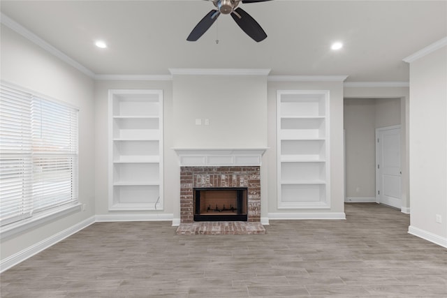 unfurnished living room featuring built in shelves, crown molding, light wood-type flooring, and a brick fireplace