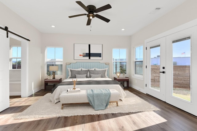 bedroom featuring ceiling fan, access to exterior, wood-type flooring, french doors, and a barn door