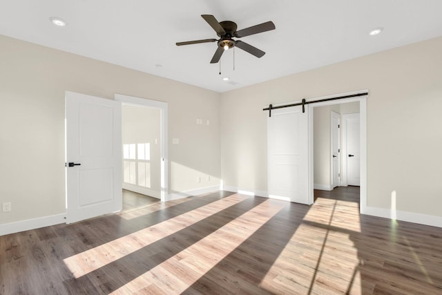 unfurnished bedroom with dark hardwood / wood-style floors, a barn door, and ceiling fan