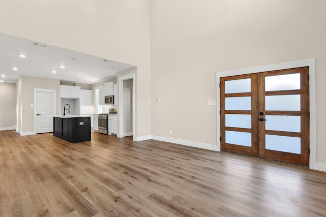 unfurnished living room with sink, a towering ceiling, light hardwood / wood-style floors, and french doors