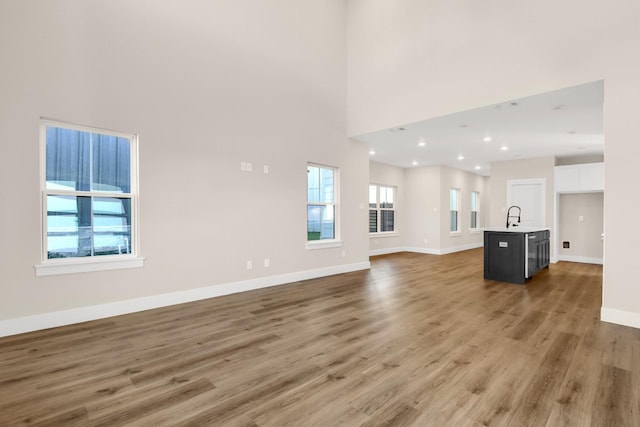 unfurnished living room featuring sink, hardwood / wood-style floors, and a high ceiling