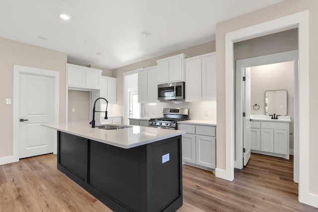 kitchen with appliances with stainless steel finishes, tasteful backsplash, white cabinetry, sink, and a center island with sink