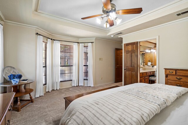 carpeted bedroom with ceiling fan, crown molding, ensuite bathroom, and a tray ceiling