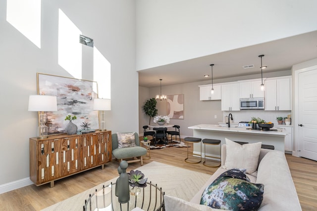 living room with an inviting chandelier, sink, a high ceiling, and light wood-type flooring