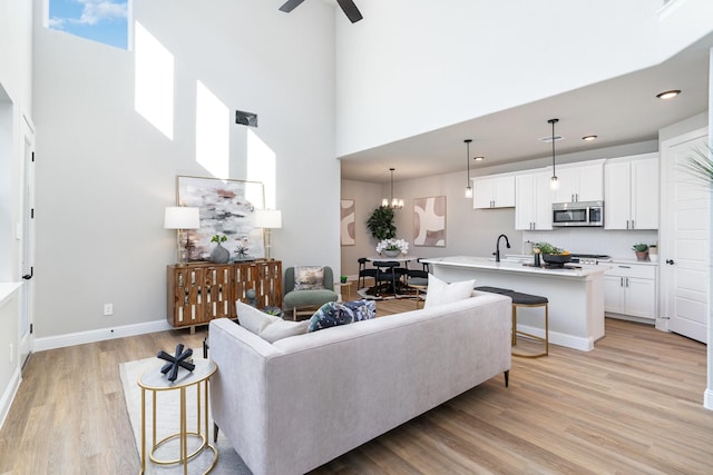 living room featuring sink, a towering ceiling, ceiling fan with notable chandelier, and light wood-type flooring