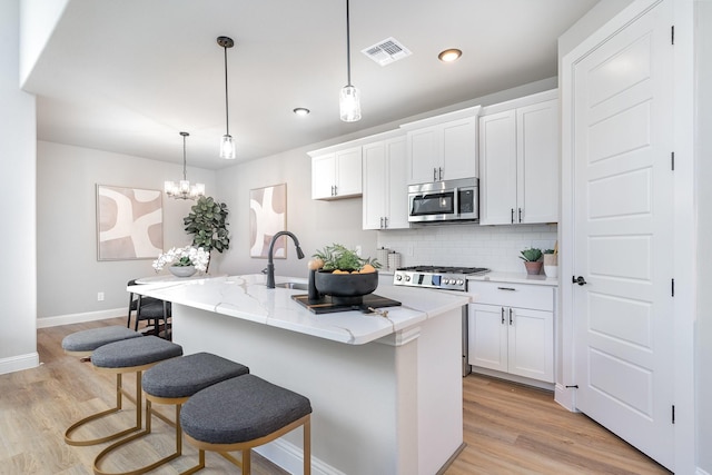 kitchen with hanging light fixtures, a center island with sink, and white cabinets