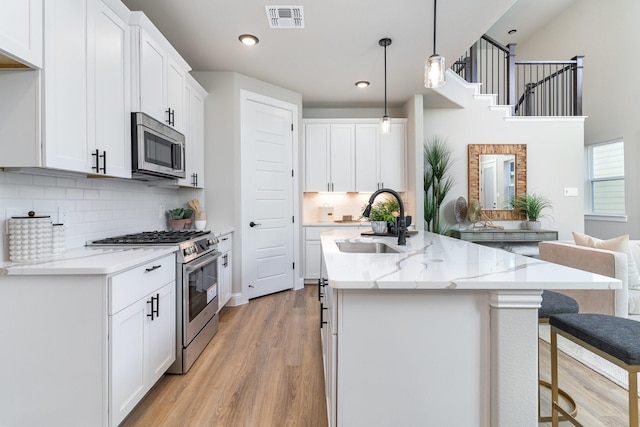 kitchen with sink, decorative light fixtures, stainless steel appliances, light stone countertops, and white cabinets