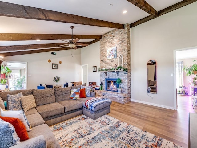 living room with vaulted ceiling with beams, light wood-type flooring, a brick fireplace, and ceiling fan