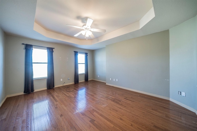 unfurnished room featuring a tray ceiling, ceiling fan, and dark wood-type flooring