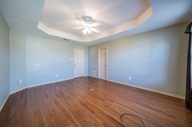 spare room with dark hardwood / wood-style flooring, a tray ceiling, and ceiling fan