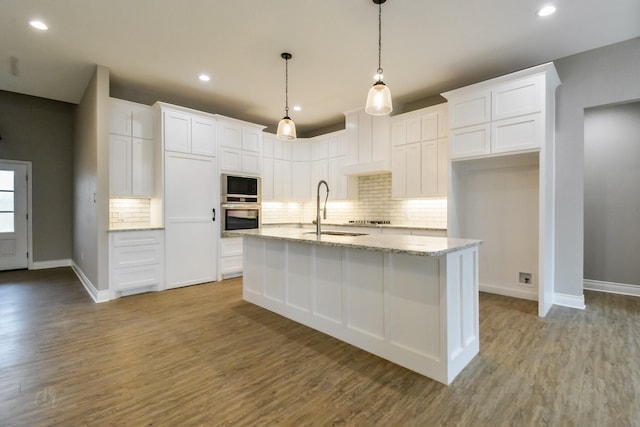 kitchen with sink, hanging light fixtures, oven, a kitchen island with sink, and white cabinets