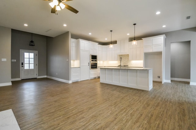 kitchen featuring built in microwave, oven, a kitchen island with sink, and white cabinets