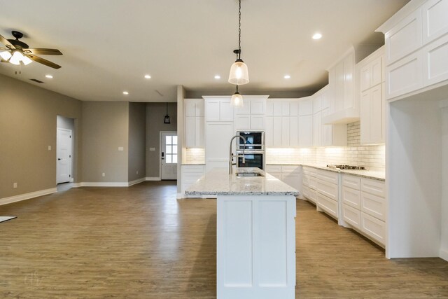 kitchen with light hardwood / wood-style flooring, a center island with sink, white cabinets, and decorative light fixtures