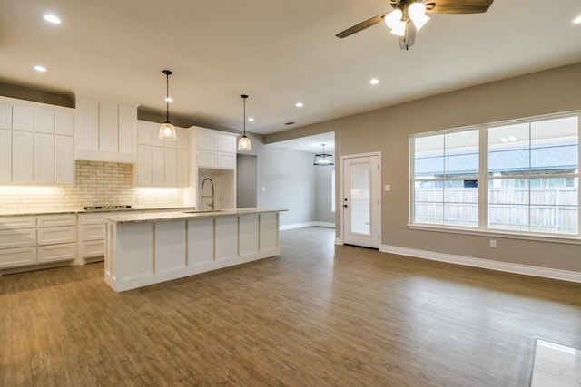 kitchen featuring a kitchen island with sink, sink, backsplash, and white cabinets