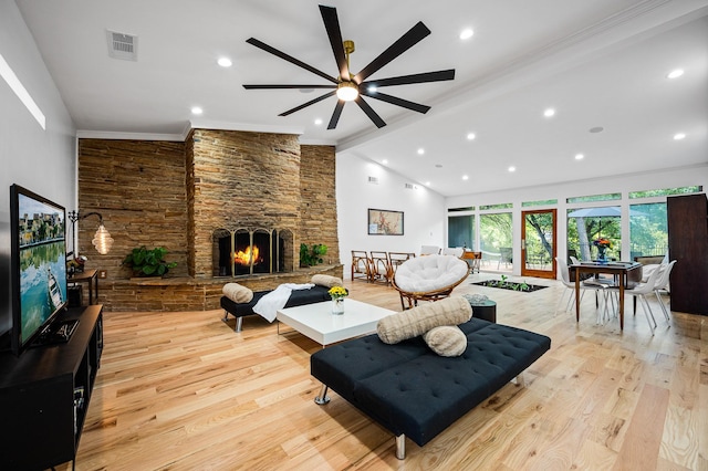 living room with ceiling fan, a stone fireplace, crown molding, vaulted ceiling, and light wood-type flooring