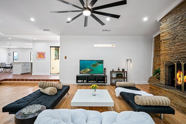 living room with light wood-type flooring, a stone fireplace, and ceiling fan