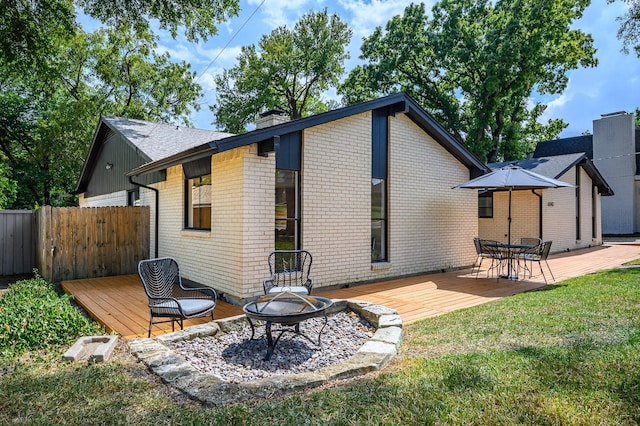 rear view of property featuring a fire pit, a lawn, and a wooden deck