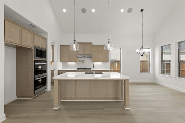 kitchen with stainless steel microwave, sink, decorative light fixtures, decorative backsplash, and a center island with sink