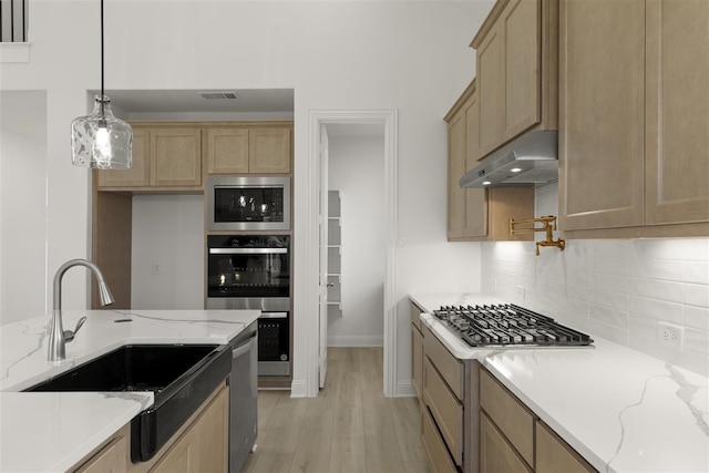 kitchen with pendant lighting, sink, light wood-type flooring, light stone counters, and stainless steel appliances