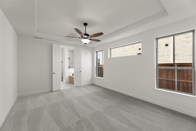 unfurnished bedroom with connected bathroom, light colored carpet, a raised ceiling, and ceiling fan