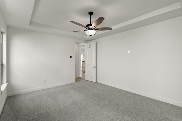 carpeted spare room featuring ceiling fan and a raised ceiling