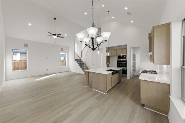 kitchen with ceiling fan with notable chandelier, stainless steel appliances, decorative light fixtures, a center island with sink, and light hardwood / wood-style flooring